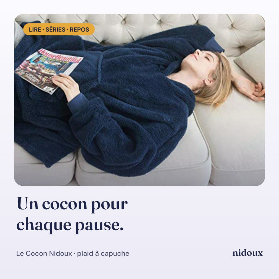 Femme allongée sur un canapé qui lit dans son plaid à capuche Nidoux